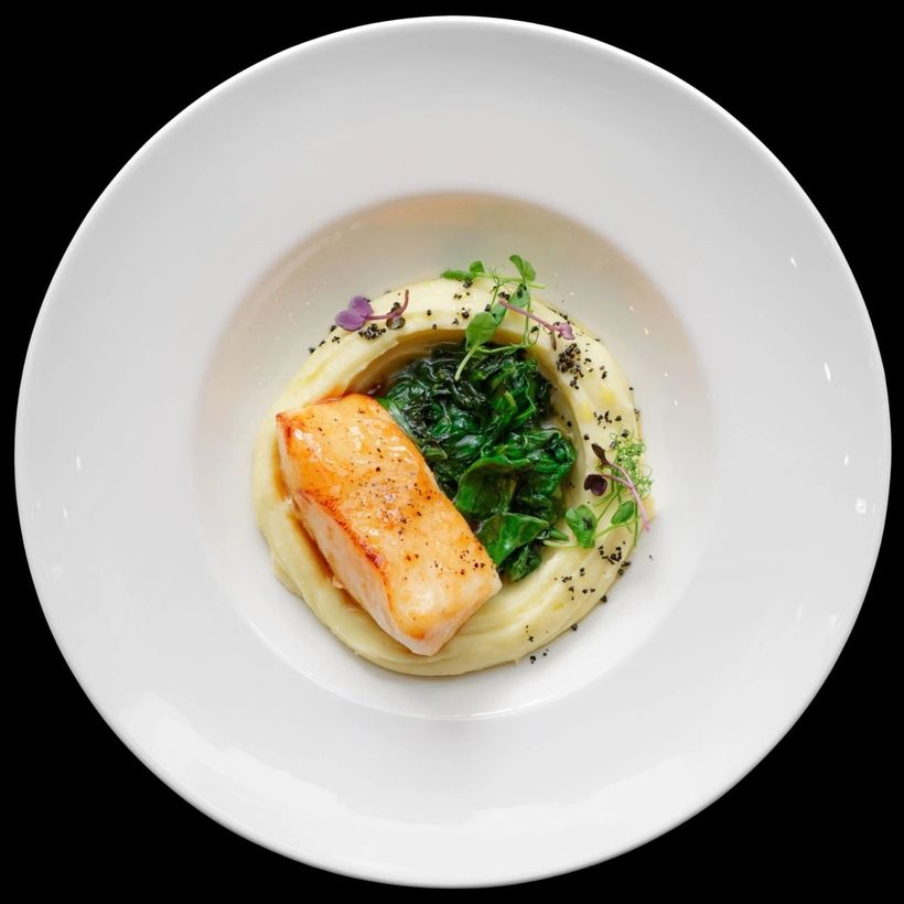 Salmon over purée with wilted greens on a wide white plate